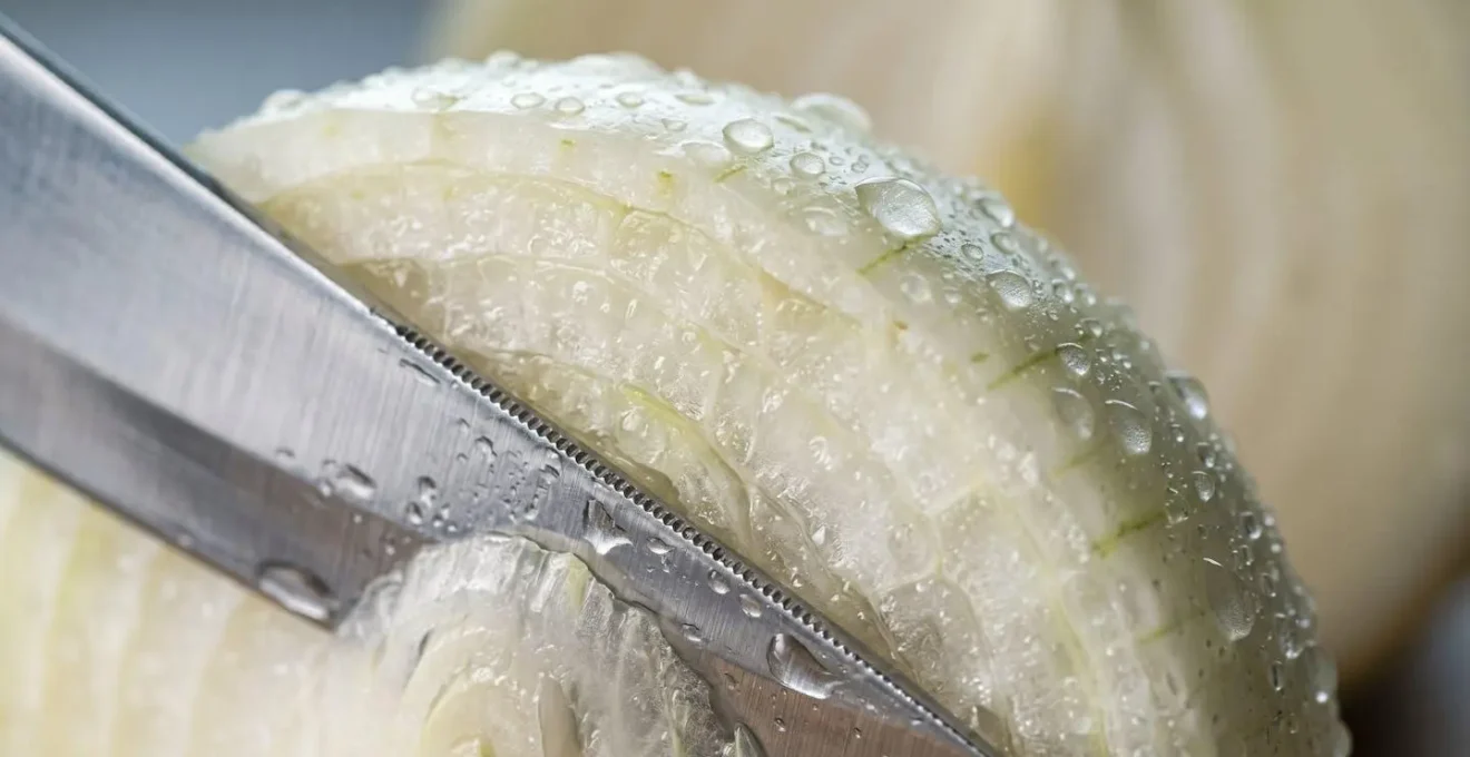 Gros plan macro sur une lame de couteau aiguisé tranchant proprement un oignon avec des gouttelettes d'eau visibles