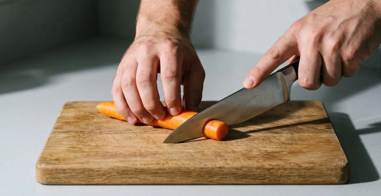 Gros plan sur une main en position griffe sécurisée guidant un couteau lors de la découpe de légumes