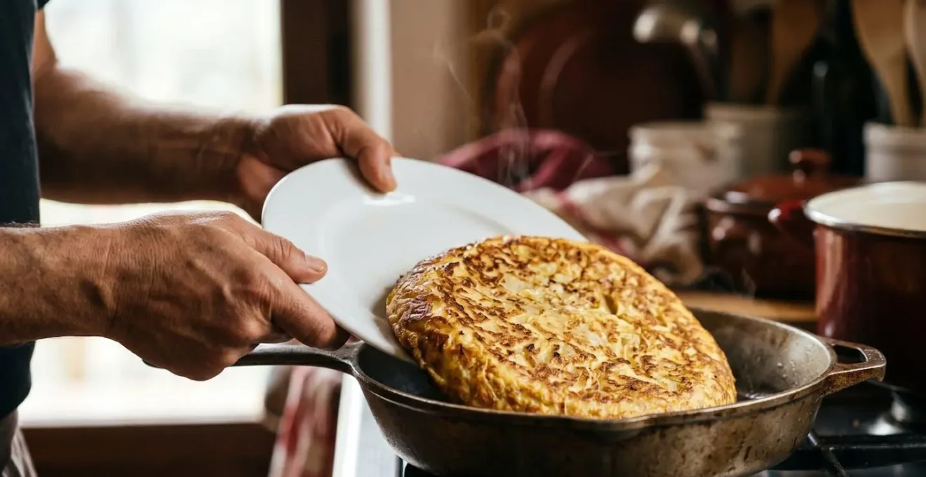 Gros plan sur des mains tenant une assiette au-dessus d'une poêle pour retourner une tortilla dorée
