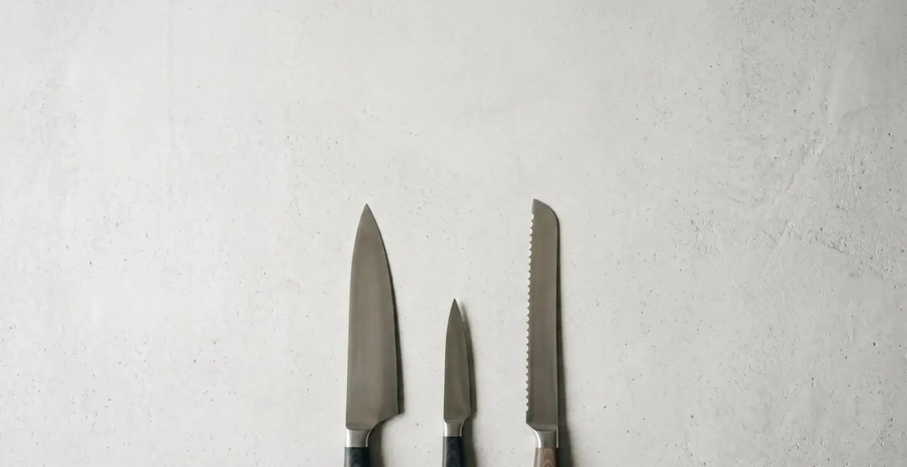 Mise en scène épurée de trois couteaux essentiels disposés sur une surface minimaliste